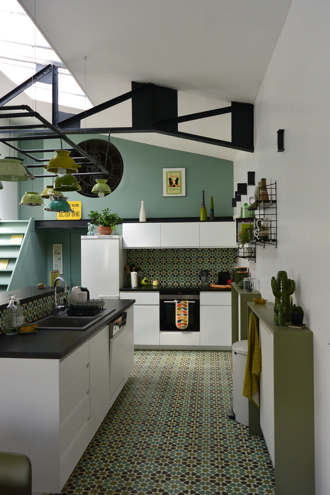 Стильный дизайн: угловая кухня-гостиная в стиле фьюжн с накладной мойкой, плоскими фасадами, белыми фасадами, зеленым фартуком, белой техникой, островом и зеленым полом - последний тренд