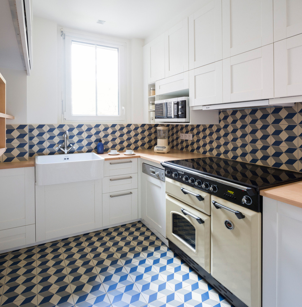 パリにあるトランジショナルスタイルのおしゃれなキッチン (白いキャビネット、木材カウンター、青いキッチンパネル、セラミックタイルのキッチンパネル、カラー調理設備、セラミックタイルの床、青い床、エプロンフロントシンク、シェーカースタイル扉のキャビネット、アイランドなし、ベージュのキッチンカウンター、窓) の写真
