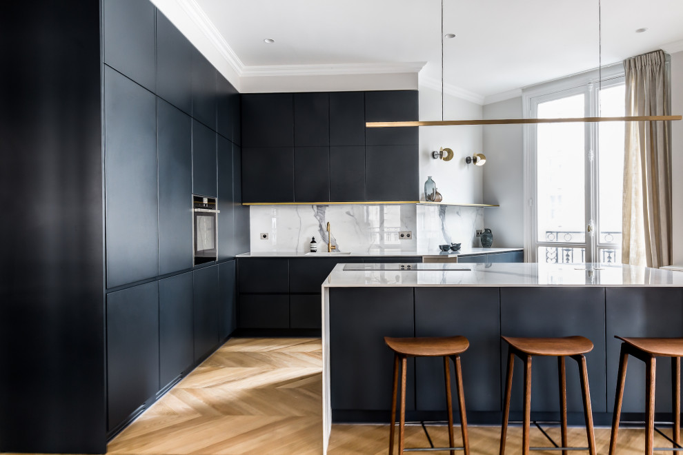 Moderne Küche in L-Form mit Unterbauwaschbecken, flächenbündigen Schrankfronten, schwarzen Schränken, Küchenrückwand in Weiß, schwarzen Elektrogeräten, braunem Holzboden, Kücheninsel, braunem Boden und weißer Arbeitsplatte in Paris
