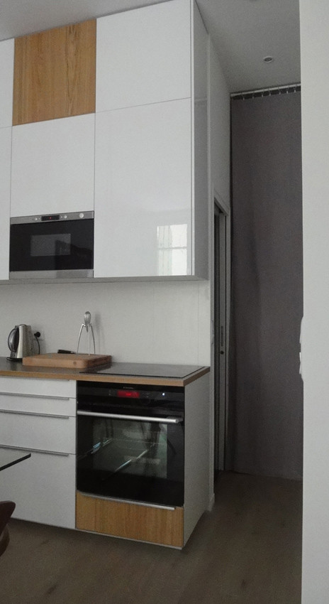 Modern inredning av ett litet linjärt kök med öppen planlösning, med en undermonterad diskho, luckor med profilerade fronter, vita skåp, laminatbänkskiva, vitt stänkskydd, stänkskydd i keramik, svarta vitvaror och ljust trägolv