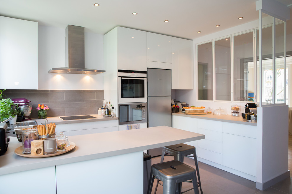 Стильный дизайн: п-образная кухня-гостиная среднего размера в современном стиле с плоскими фасадами, белыми фасадами, серым фартуком, полуостровом и барной стойкой - последний тренд