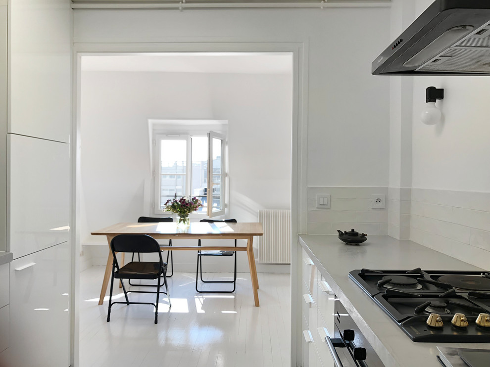Идея дизайна: большая отдельная, угловая кухня в современном стиле с деревянным полом, белым полом, белыми фасадами, белым фартуком, фартуком из плитки кабанчик, черной техникой и белой столешницей
