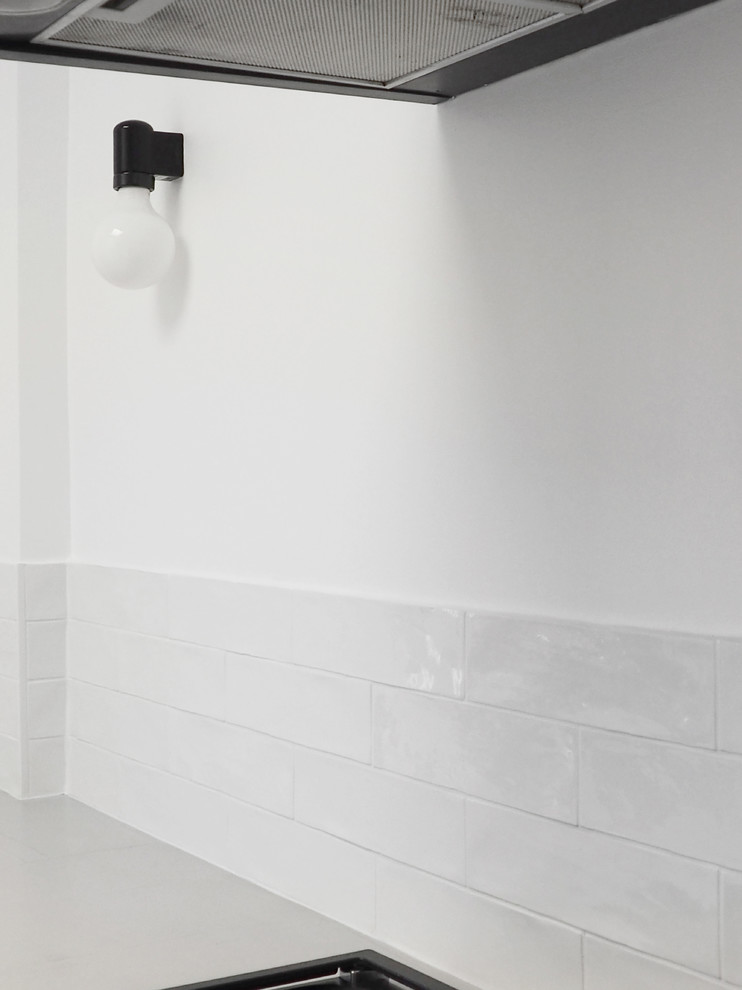 Modelo de cocinas en L contemporánea grande cerrada con puertas de armario blancas, salpicadero blanco, salpicadero de azulejos tipo metro, electrodomésticos negros, suelo de madera pintada, suelo blanco y encimeras blancas