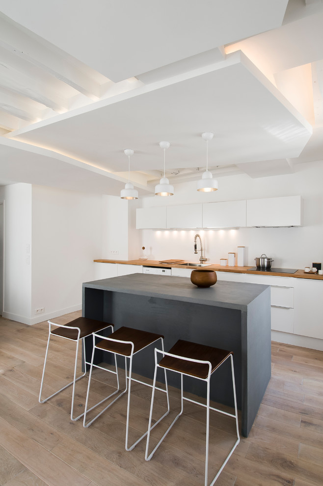 На фото: параллельная кухня среднего размера в скандинавском стиле с плоскими фасадами, белыми фасадами, светлым паркетным полом, островом и обеденным столом с