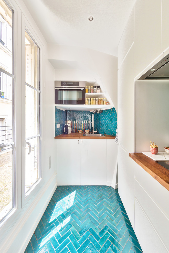 パリにある高級な中くらいな地中海スタイルのおしゃれなキッチン (白いキャビネット、木材カウンター、青いキッチンパネル、テラコッタタイルのキッチンパネル、アイランドなし、青い床、シングルシンク、インセット扉のキャビネット、パネルと同色の調理設備、テラコッタタイルの床、茶色いキッチンカウンター) の写真