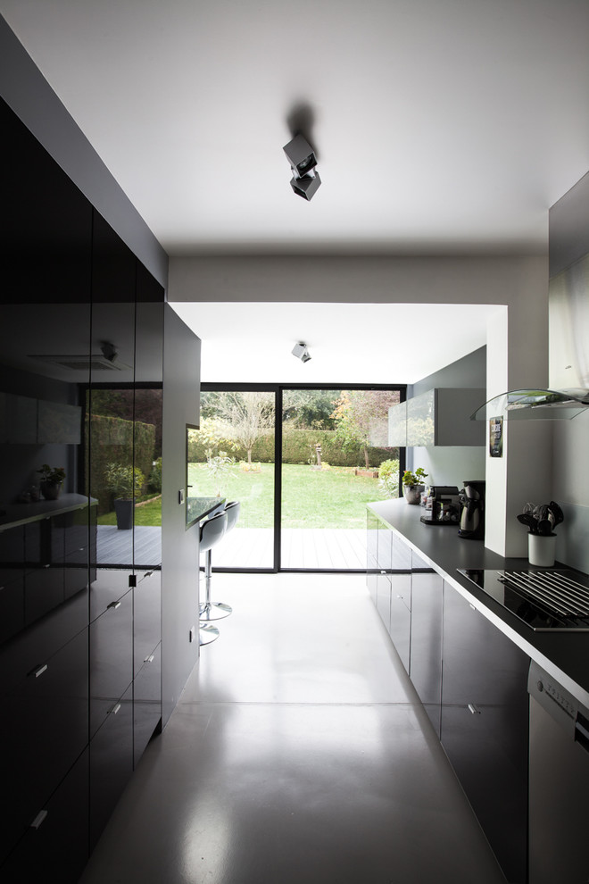 Zweizeilige, Große Moderne Wohnküche mit grauen Schränken, Küchenrückwand in Weiß, Glasrückwand, Betonboden und Halbinsel in Paris