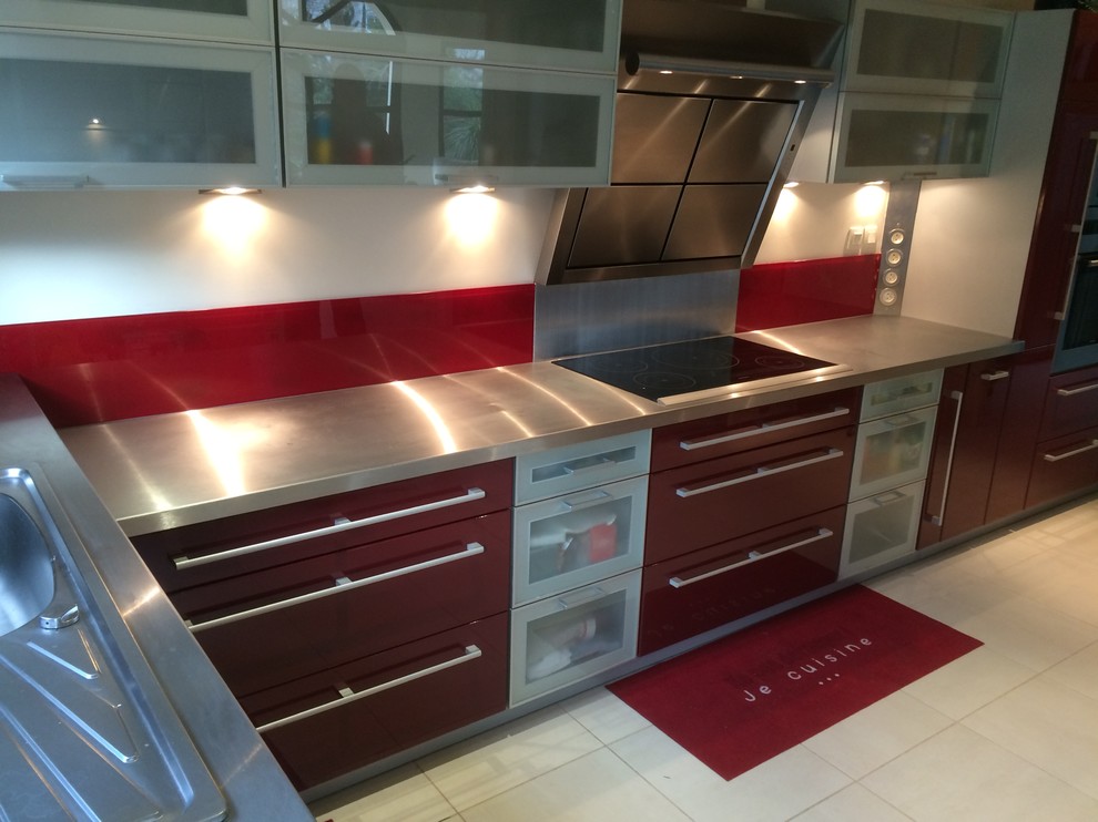 Contemporary kitchen in Le Havre with a single-bowl sink, stainless steel worktops, red splashback, glass sheet splashback and stainless steel appliances.