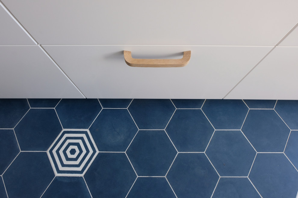 Cette image montre une cuisine parallèle design fermée avec des portes de placard blanches, un plan de travail en stratifié, une crédence bleue, une crédence en carreau de ciment, carreaux de ciment au sol et un sol bleu.