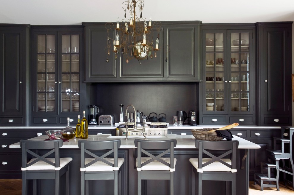 Inspiration for a mid-sized timeless galley light wood floor and brown floor kitchen remodel in Paris with marble countertops, stainless steel appliances, an island, white countertops, glass-front cabinets, black cabinets and black backsplash