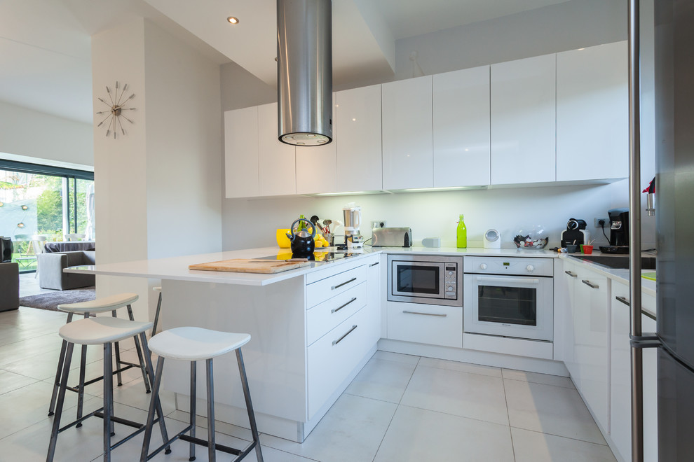 Идея дизайна: п-образная кухня-гостиная в современном стиле с плоскими фасадами, белыми фасадами, белой техникой и полуостровом
