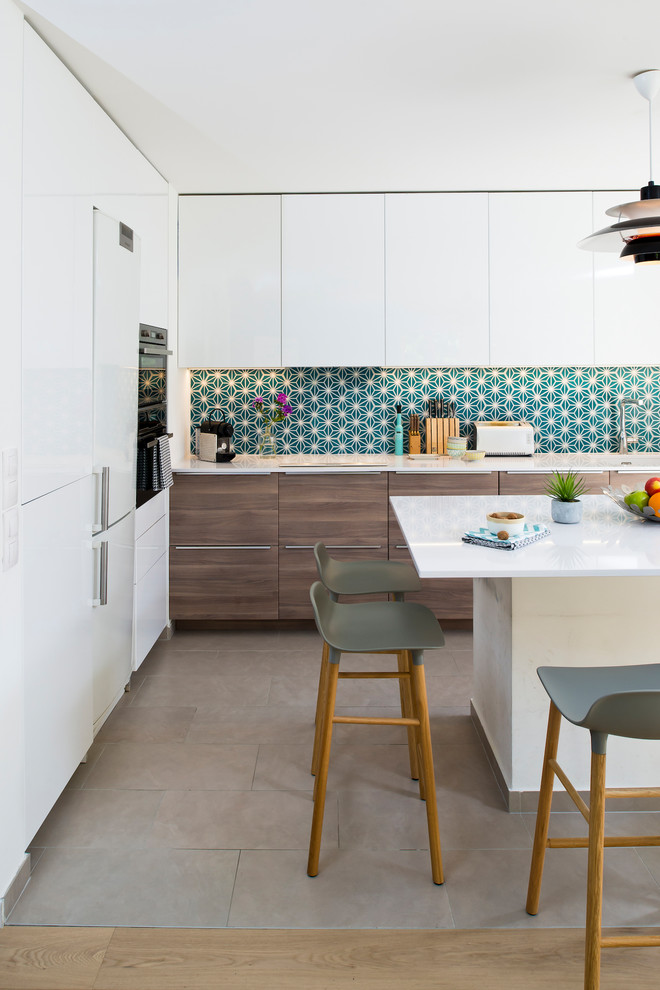 Inspiration för ett funkis l-kök, med släta luckor, vita skåp, grönt stänkskydd, betonggolv, en köksö och grått golv