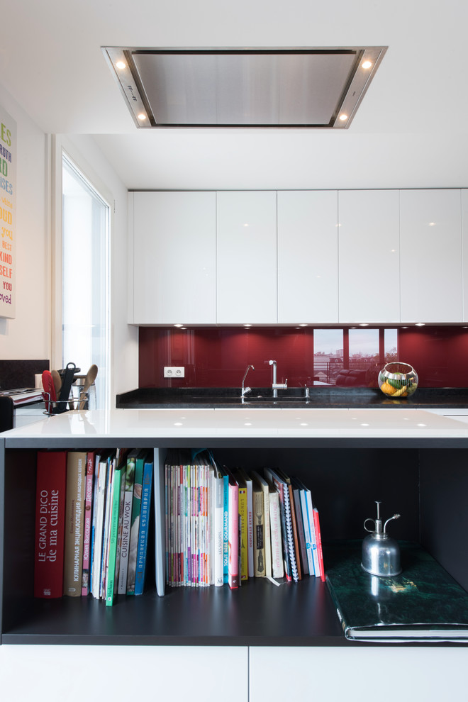 Bild på ett mellanstort funkis kök, med en integrerad diskho, luckor med profilerade fronter, vita skåp, granitbänkskiva, rött stänkskydd, stänkskydd i glaskakel, rostfria vitvaror, ljust trägolv och en köksö