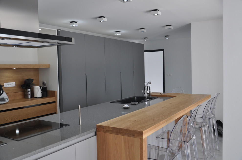 Inredning av ett modernt mycket stort grå linjärt grått kök med öppen planlösning, med en undermonterad diskho, släta luckor, grå skåp, bänkskiva i kvartsit, integrerade vitvaror, klinkergolv i keramik, en köksö och grått golv