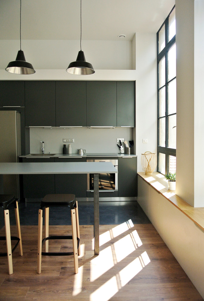 Imagen de cocina comedor lineal contemporánea de tamaño medio con armarios con paneles lisos, electrodomésticos de acero inoxidable, suelo de madera en tonos medios, una isla, salpicadero verde y con blanco y negro