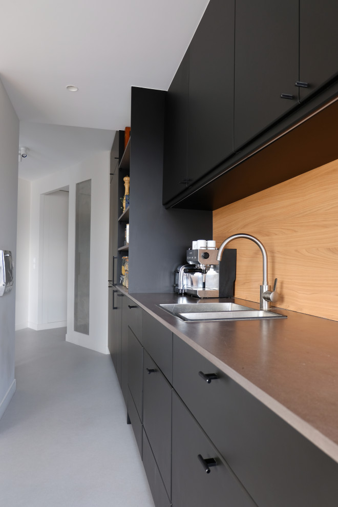 Modern inredning av ett mellanstort grå linjärt grått kök med öppen planlösning, med en undermonterad diskho, släta luckor, svarta skåp, beige stänkskydd, stänkskydd i trä, svarta vitvaror, linoleumgolv och grått golv