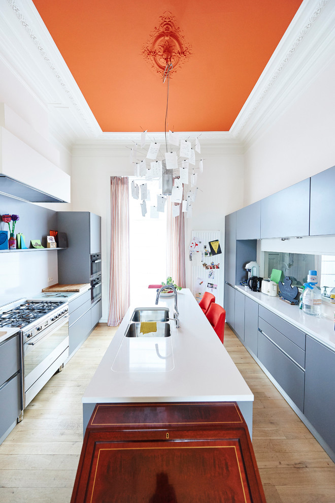 Moderne Küche mit flächenbündigen Schrankfronten, blauen Schränken, Küchenrückwand in Weiß, Küchengeräten aus Edelstahl, hellem Holzboden und Kücheninsel in Brüssel