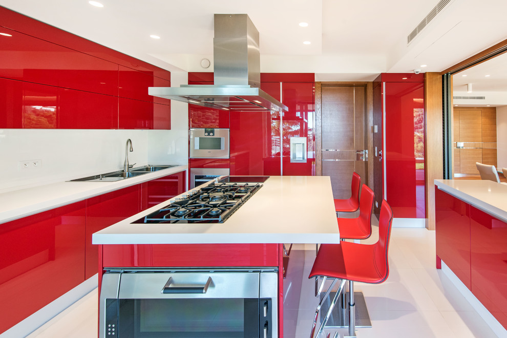 Cette image montre une cuisine design en U fermée avec un évier 2 bacs, un placard à porte plane, des portes de placard rouges, un électroménager en acier inoxydable, îlot et un sol blanc.