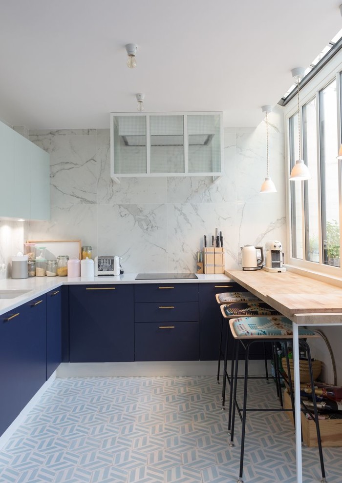 Стильный дизайн: п-образная кухня в современном стиле с обеденным столом, врезной мойкой, плоскими фасадами, синими фасадами, белым фартуком, белым полом и барной стойкой - последний тренд