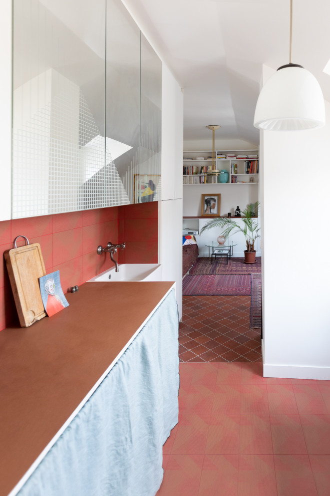 Cette photo montre une cuisine ouverte linéaire tendance avec un évier de ferme, plan de travail carrelé, une crédence rouge, une crédence en terre cuite, un sol en carrelage de céramique, un sol rouge et un plan de travail rose.