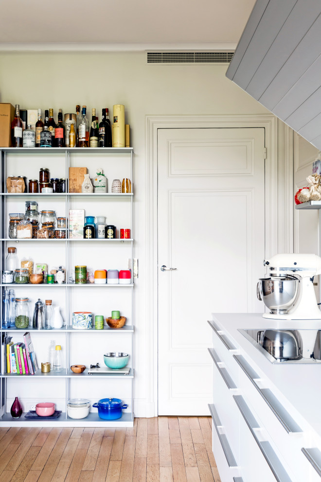 Foto på ett stort vintage vit linjärt kök med öppen planlösning, med en köksö, en undermonterad diskho, släta luckor, vita skåp, vitt stänkskydd, rostfria vitvaror och ljust trägolv