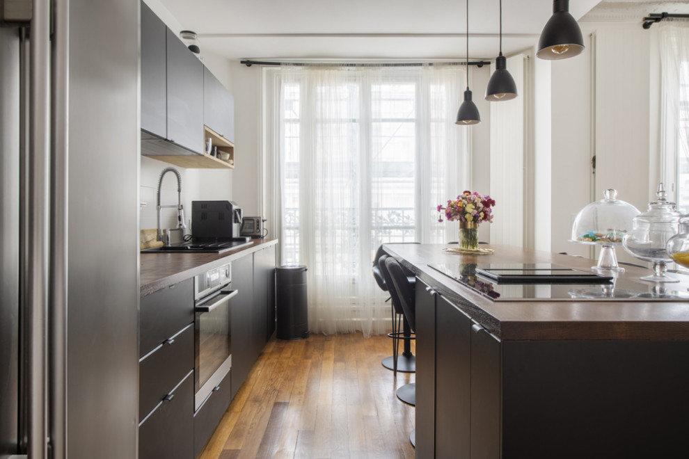 パリにあるお手頃価格の中くらいなコンテンポラリースタイルのおしゃれなキッチン (アンダーカウンターシンク、フラットパネル扉のキャビネット、黒いキャビネット、木材カウンター、白いキッチンパネル、木材のキッチンパネル、シルバーの調理設備、無垢フローリング、茶色い床、茶色いキッチンカウンター) の写真