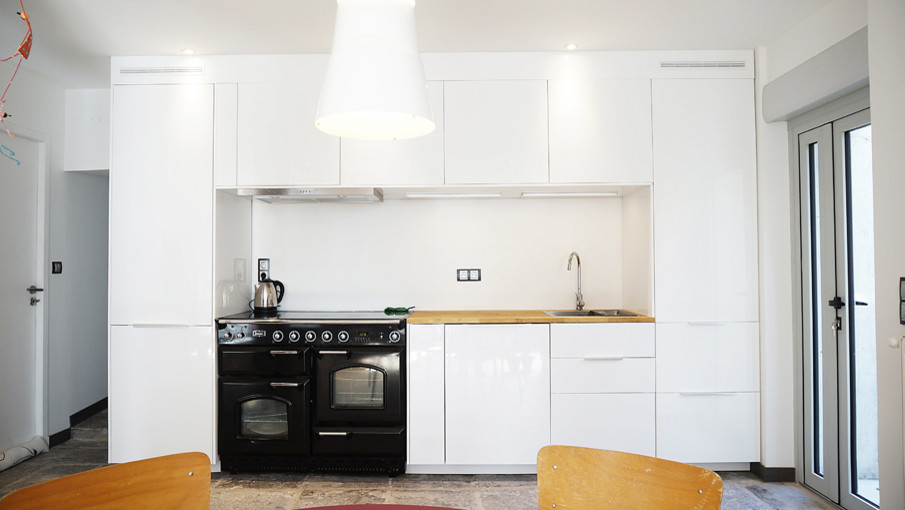 Idéer för att renovera ett litet funkis linjärt kök med öppen planlösning, med en undermonterad diskho, vita skåp, träbänkskiva, vitt stänkskydd, svarta vitvaror och klinkergolv i terrakotta