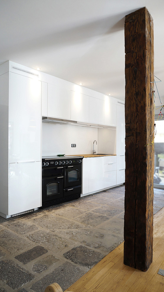 Стильный дизайн: прямая кухня-гостиная среднего размера в современном стиле с врезной мойкой, белыми фасадами, деревянной столешницей, белым фартуком, черной техникой и полом из терракотовой плитки - последний тренд