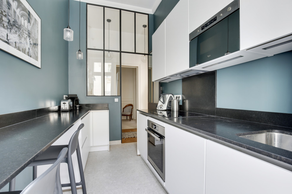 This is an example of a medium sized contemporary single-wall enclosed kitchen in Paris with a submerged sink, beaded cabinets, white cabinets, quartz worktops, black splashback, stainless steel appliances, terrazzo flooring, beige floors and black worktops.