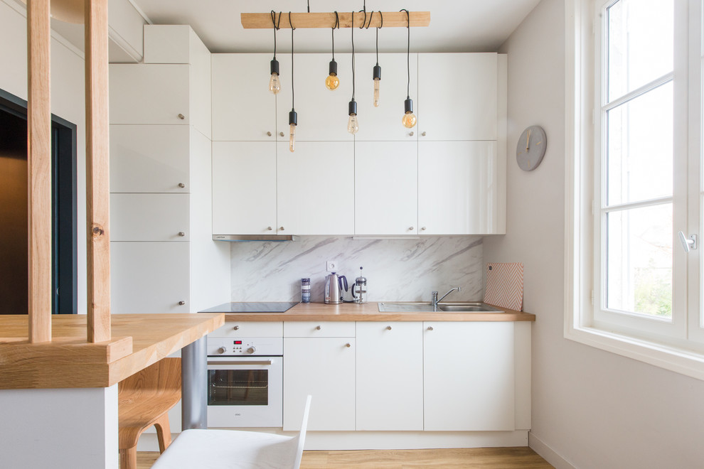 Inredning av ett minimalistiskt kök, med en nedsänkt diskho, släta luckor, vita skåp, träbänkskiva, vitt stänkskydd, stänkskydd i marmor, vita vitvaror, ljust trägolv och beiget golv