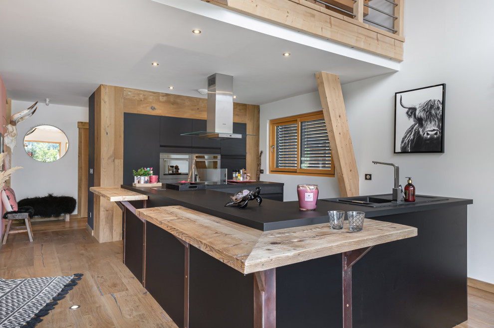 Open concept kitchen - rustic light wood floor open concept kitchen idea in Lille with a drop-in sink, flat-panel cabinets, black cabinets, an island and black countertops