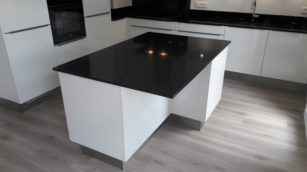 Photo of a medium sized contemporary l-shaped open plan kitchen in Other with an integrated sink, flat-panel cabinets, white cabinets, quartz worktops, black splashback, glass sheet splashback, stainless steel appliances, light hardwood flooring and an island.