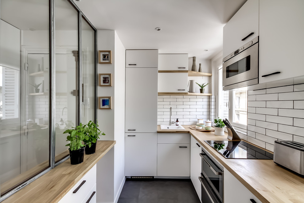 Cette image montre une cuisine encastrable nordique en U fermée et de taille moyenne avec un placard à porte plane, des portes de placard blanches, un plan de travail en bois, une crédence blanche, une crédence en carrelage métro, un sol en ardoise, aucun îlot, un évier 1 bac, un sol gris et un plan de travail beige.