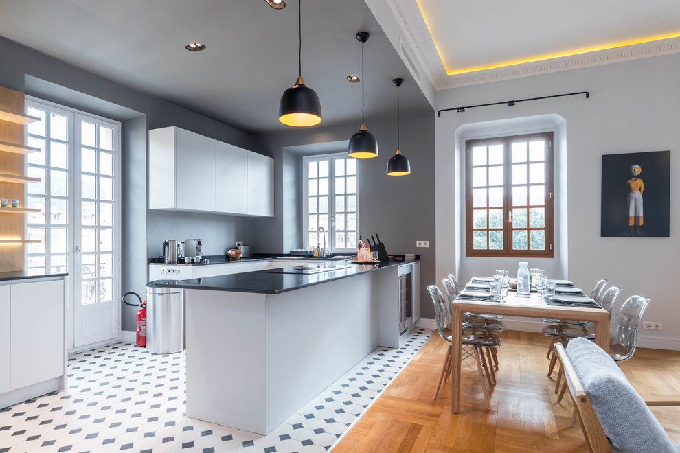 Immagine di una cucina design con ante lisce, ante bianche, penisola, pavimento multicolore, top nero e parquet e piastrelle