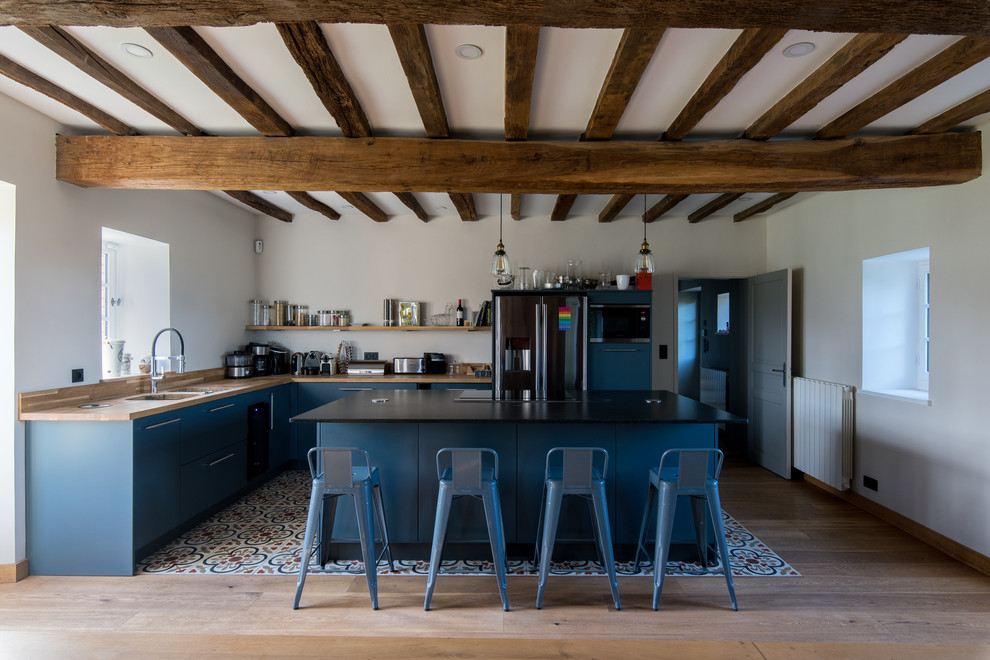 Идея дизайна: угловая кухня в стиле кантри с плоскими фасадами, синими фасадами, деревянной столешницей, черной техникой, островом, разноцветным полом, коричневой столешницей и красивой плиткой