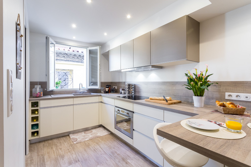 Medium sized contemporary l-shaped kitchen/diner in Nice with a submerged sink, flat-panel cabinets, white cabinets, wood worktops, stainless steel appliances and a breakfast bar.