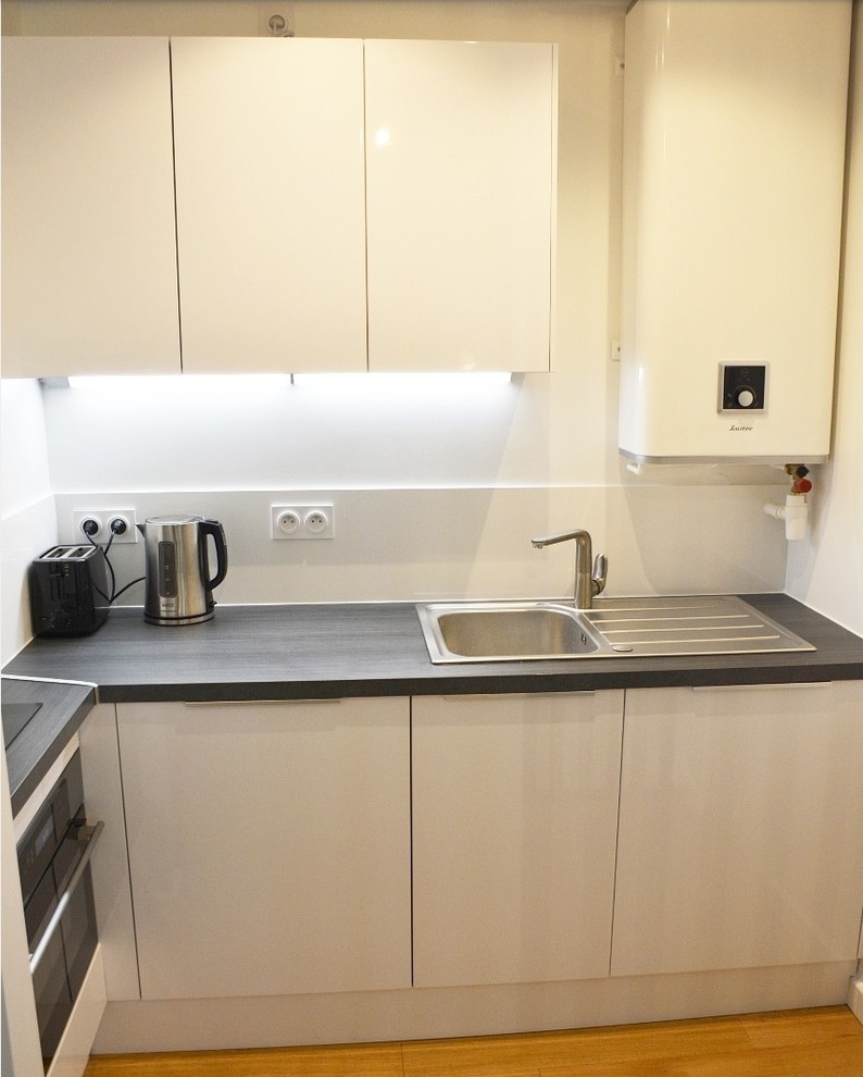 Foto på ett litet funkis grå kök, med en enkel diskho, luckor med profilerade fronter, vita skåp, laminatbänkskiva, vitt stänkskydd, stänkskydd i keramik, rostfria vitvaror och ljust trägolv