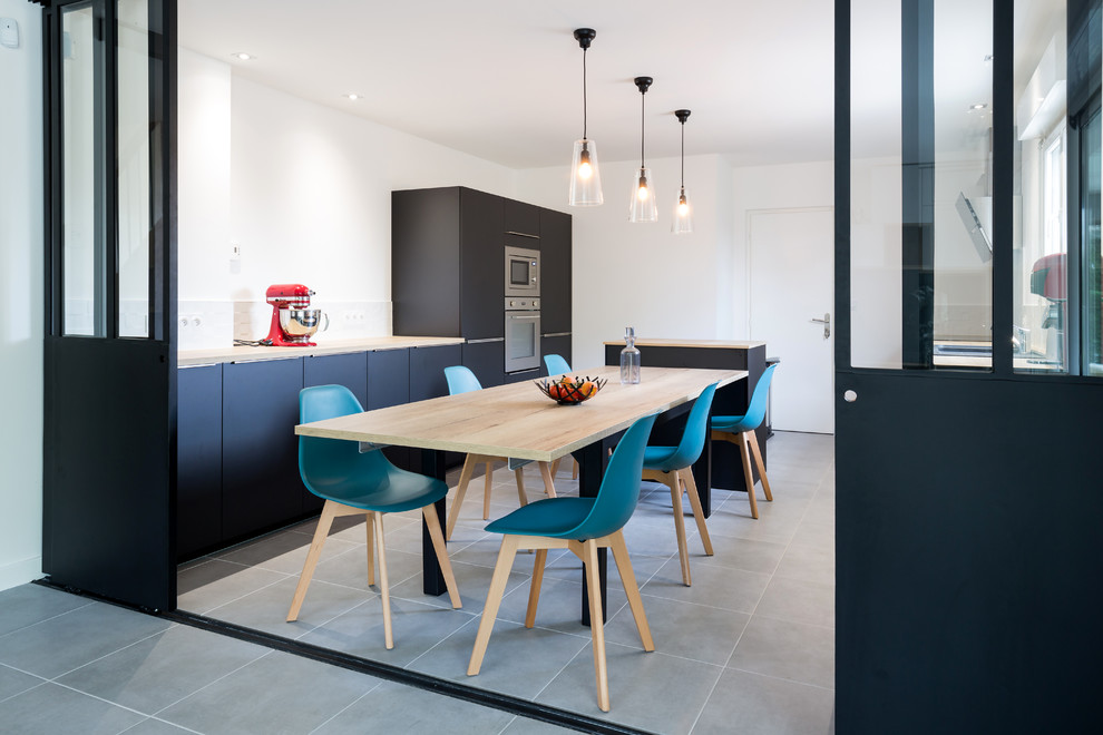 This is an example of a contemporary enclosed kitchen in Bordeaux with a built-in sink, flat-panel cabinets, black cabinets, wood worktops, white splashback, stainless steel appliances, an island, grey floors and beige worktops.