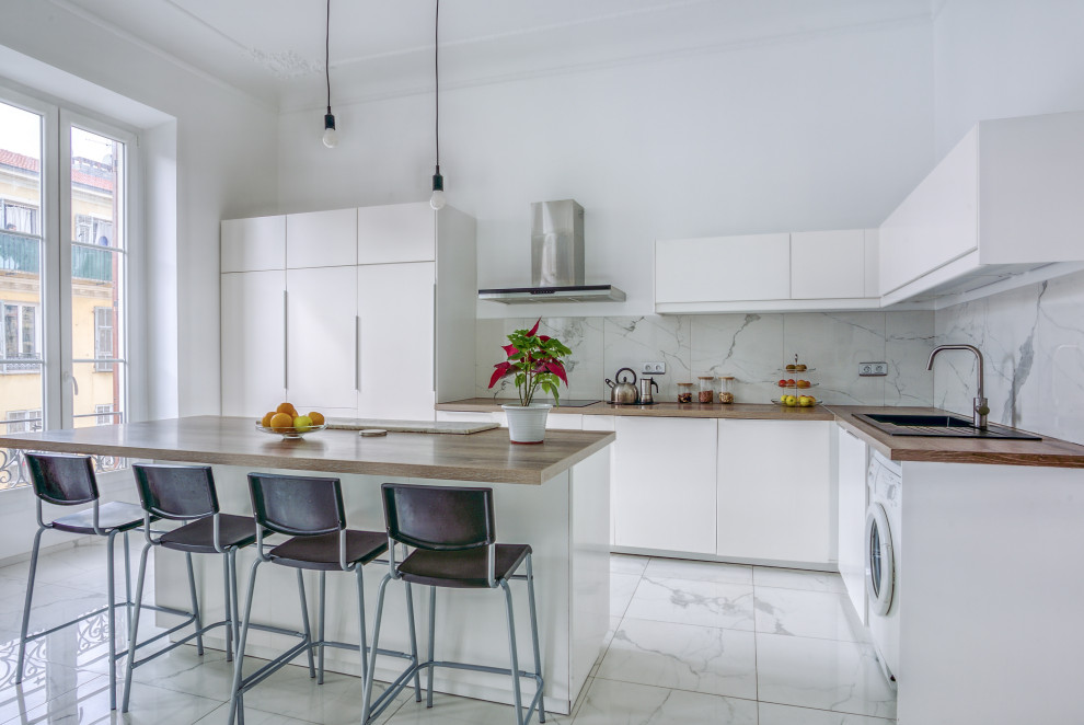This is an example of a contemporary l-shaped kitchen in Nice with a built-in sink, flat-panel cabinets, white cabinets, wood worktops, white splashback, integrated appliances, an island, white floors and brown worktops.