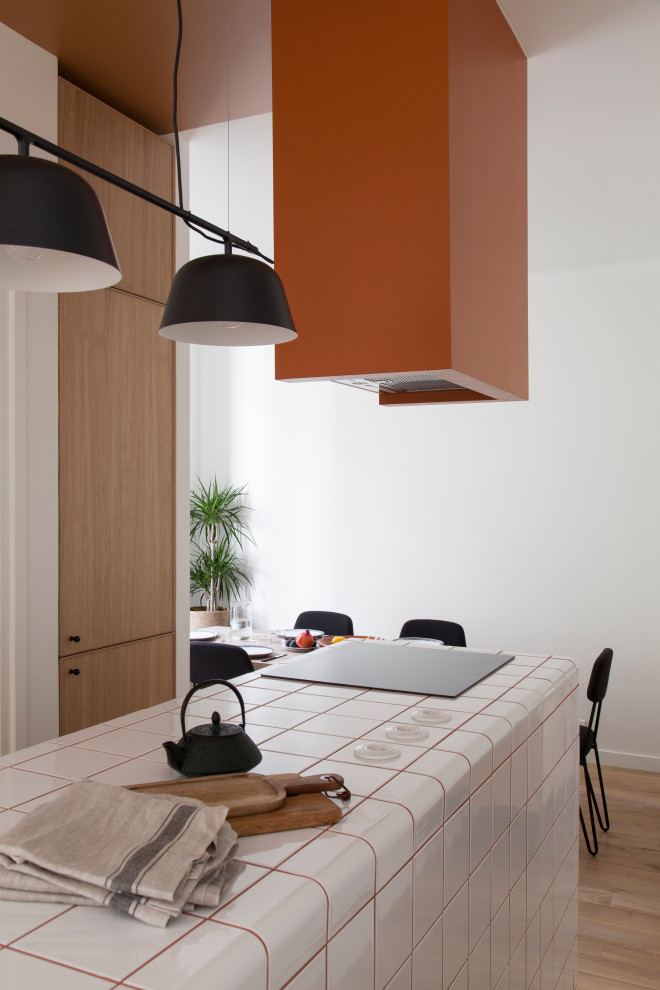 Inspiration for a medium sized scandi single-wall open plan kitchen in Paris with an integrated sink, beaded cabinets, light wood cabinets, tile countertops, grey splashback, integrated appliances, terracotta flooring, an island, brown floors and white worktops.