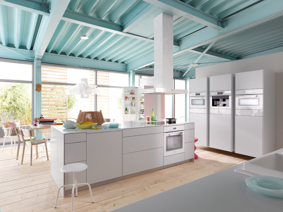Diseño de cocina contemporánea grande abierta con fregadero encastrado, puertas de armario blancas, electrodomésticos blancos, suelo de madera clara y una isla
