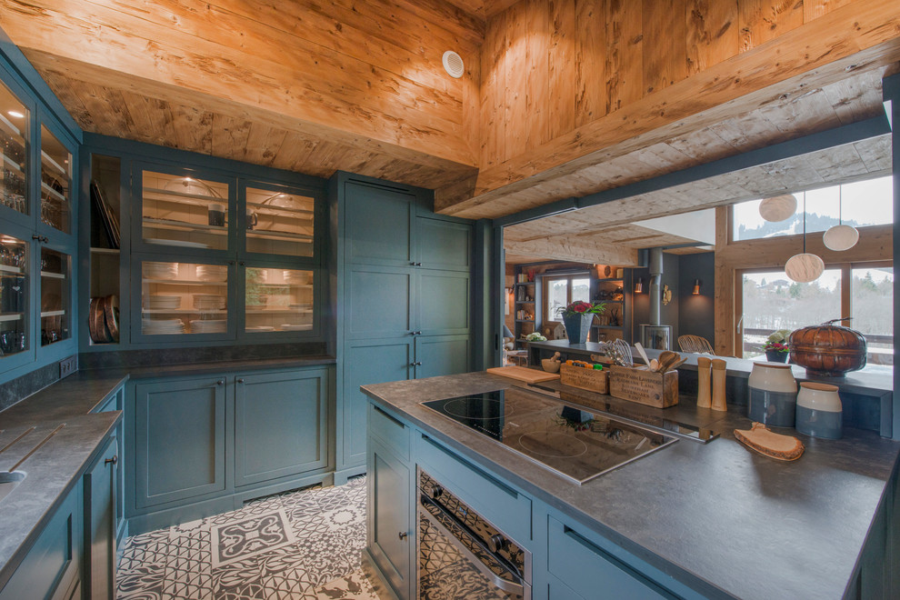 Immagine di una cucina stile rurale con ante di vetro, ante blu, paraspruzzi grigio, elettrodomestici neri e pavimento multicolore