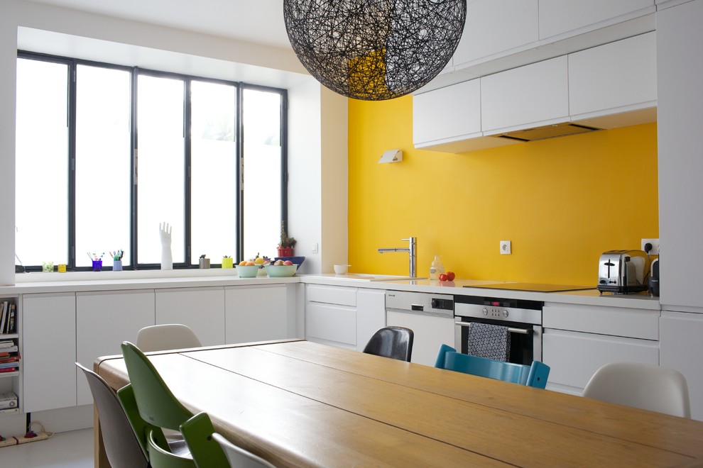 Große Moderne Wohnküche ohne Insel in L-Form mit flächenbündigen Schrankfronten, weißen Schränken, Küchengeräten aus Edelstahl und Küchenrückwand in Gelb in Paris