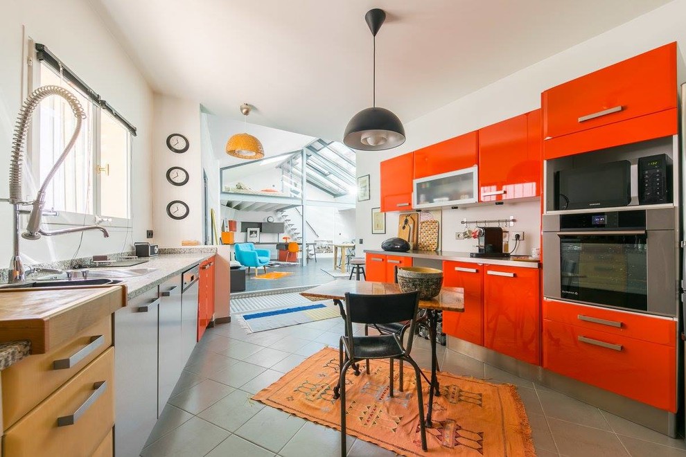Inspiration for a large bohemian galley open plan kitchen in Lille with white splashback, stainless steel appliances, no island, grey floors, a built-in sink, flat-panel cabinets, red cabinets, stainless steel worktops and cement flooring.