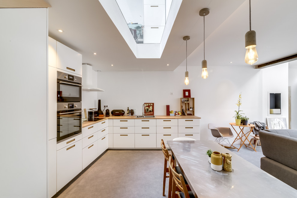 Example of a trendy l-shaped concrete floor and gray floor open concept kitchen design in Paris with flat-panel cabinets, white cabinets, wood countertops, stainless steel appliances and no island