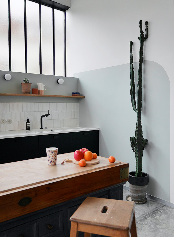 Photo of an expansive urban l-shaped open plan kitchen with a single-bowl sink, beaded cabinets, black cabinets, laminate countertops, white splashback, ceramic splashback, black appliances, concrete flooring, an island, grey floors and white worktops.