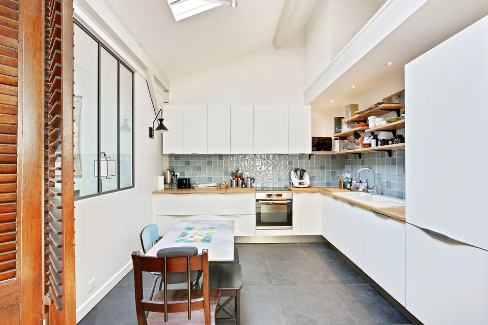 Inredning av ett modernt stort brun brunt kök, med en integrerad diskho, luckor med profilerade fronter, vita skåp, träbänkskiva, blått stänkskydd, stänkskydd i keramik, vita vitvaror, skiffergolv och grått golv