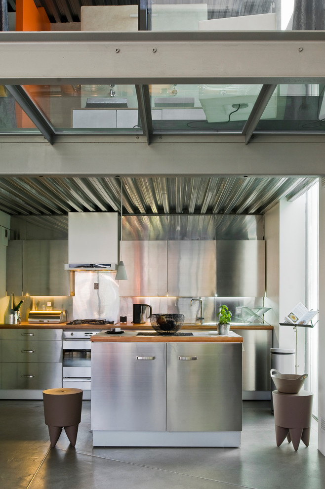 Inredning av ett industriellt mellanstort kök, med släta luckor, skåp i rostfritt stål, stänkskydd med metallisk yta, rostfria vitvaror och en köksö