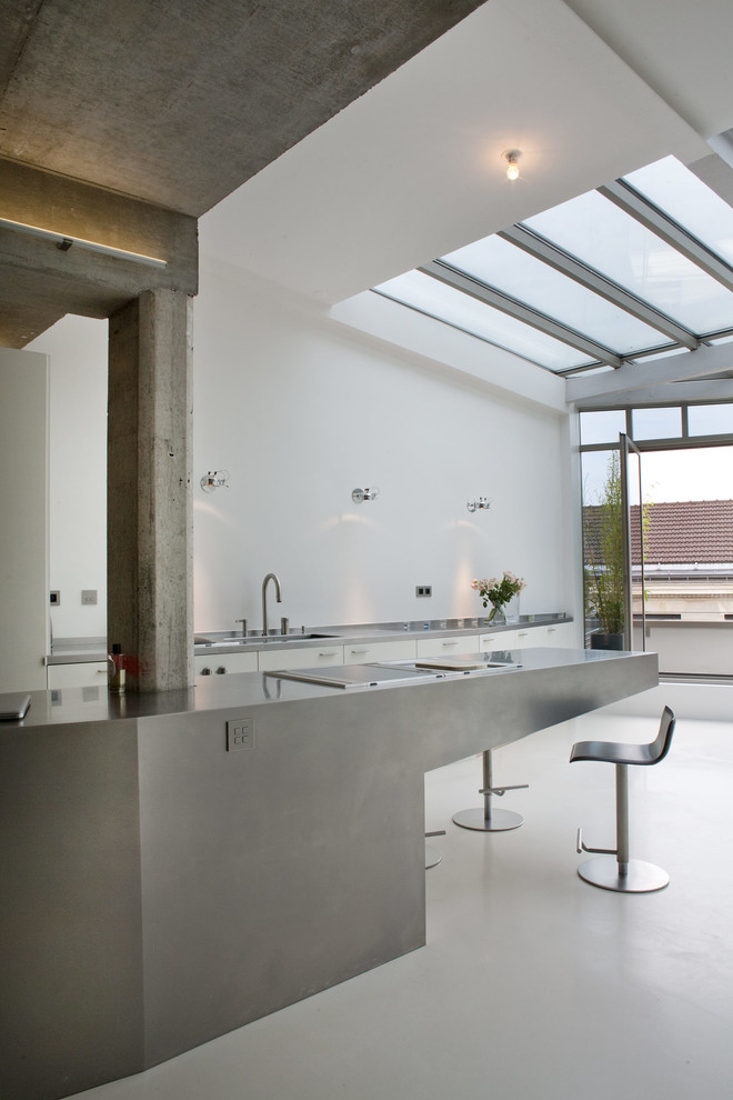 Example of a large urban galley beige floor open concept kitchen design in Paris with flat-panel cabinets, white cabinets, an island, an integrated sink, white backsplash, stainless steel appliances and gray countertops
