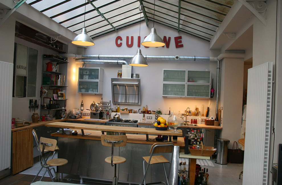 Immagine di una cucina industriale di medie dimensioni con lavello a doppia vasca, ante lisce, ante in acciaio inossidabile, top in legno, pavimento con piastrelle in ceramica e penisola