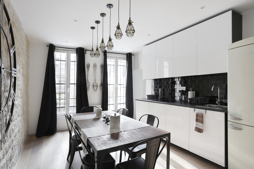 Стильный дизайн: кухня в современном стиле с обеденным столом, накладной мойкой, плоскими фасадами, черным фартуком, светлым паркетным полом, бежевым полом и черно-белыми фасадами - последний тренд